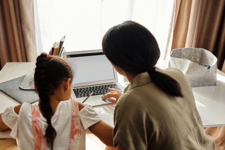 A mother helps her daughter with online learning on a laptop at home, emphasizing family education.